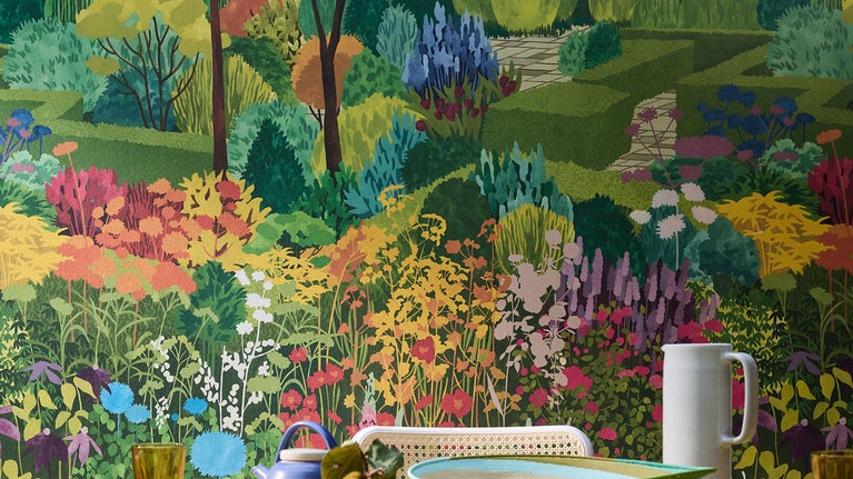 A table set for breakfast sits in front of a heavily patterned wallpaper showing a multicoloured castle garden